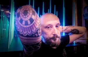 Wytatuowany mężczyzna w średnim wieku patrzy prosto w kamerę